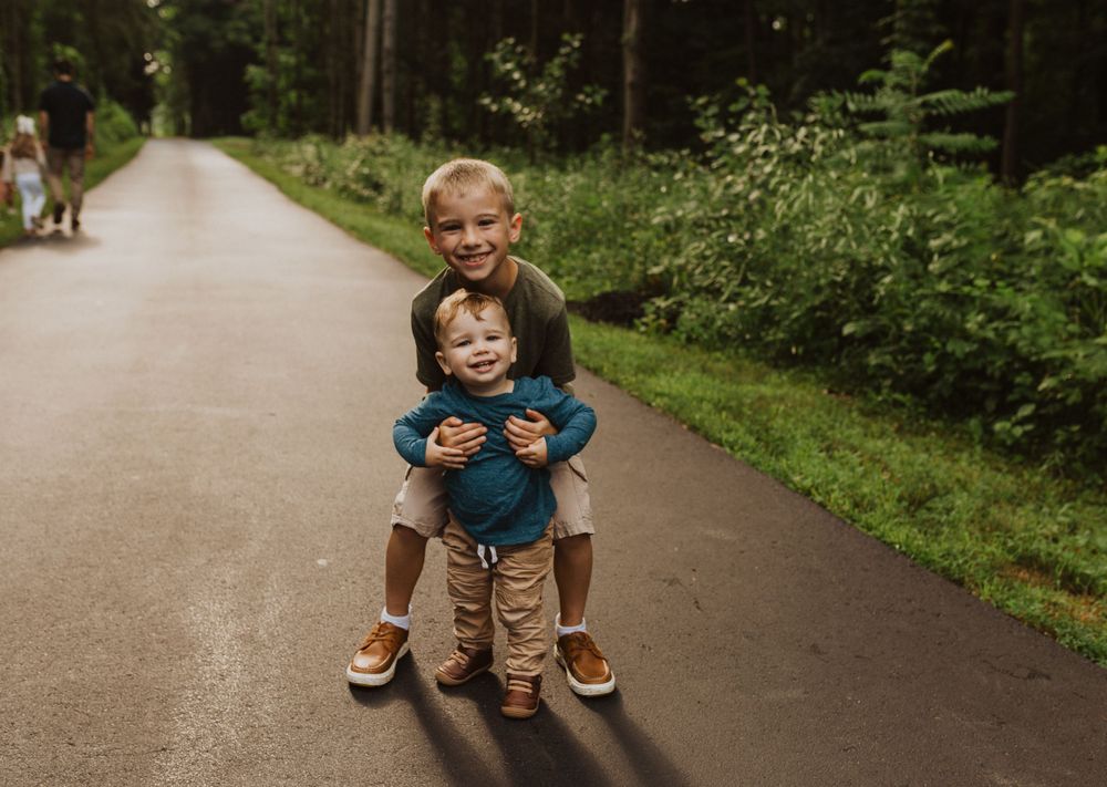 A family poses playfully on a tree-lined walking path during a summer photo session.