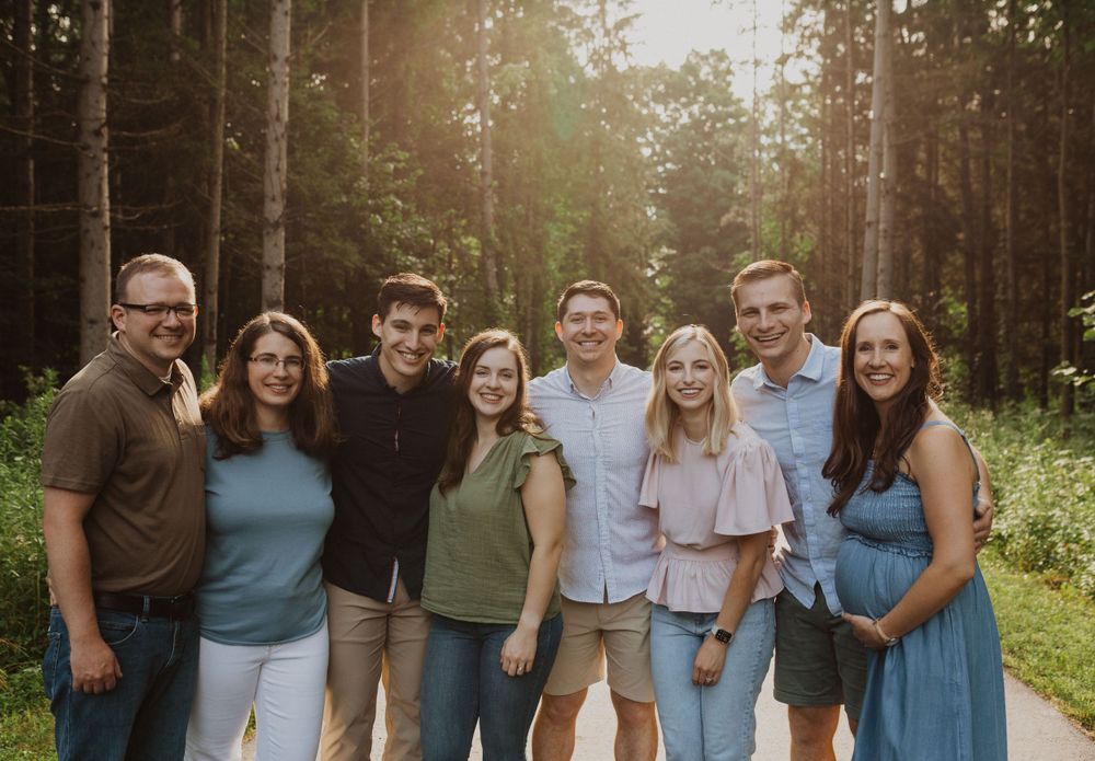 Extended family members stand together on a forest trail at sunset.