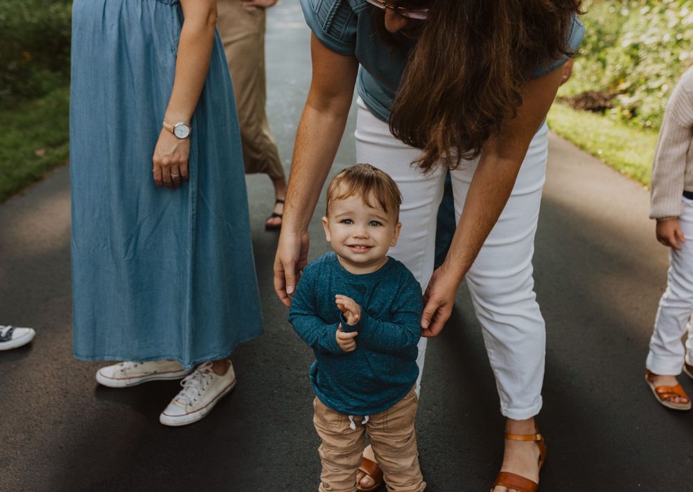 Small child in blue shirt walking on paved forest path.