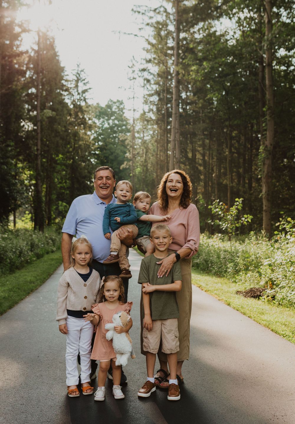 Small family group poses casually on tree-lined path in afternoon light.