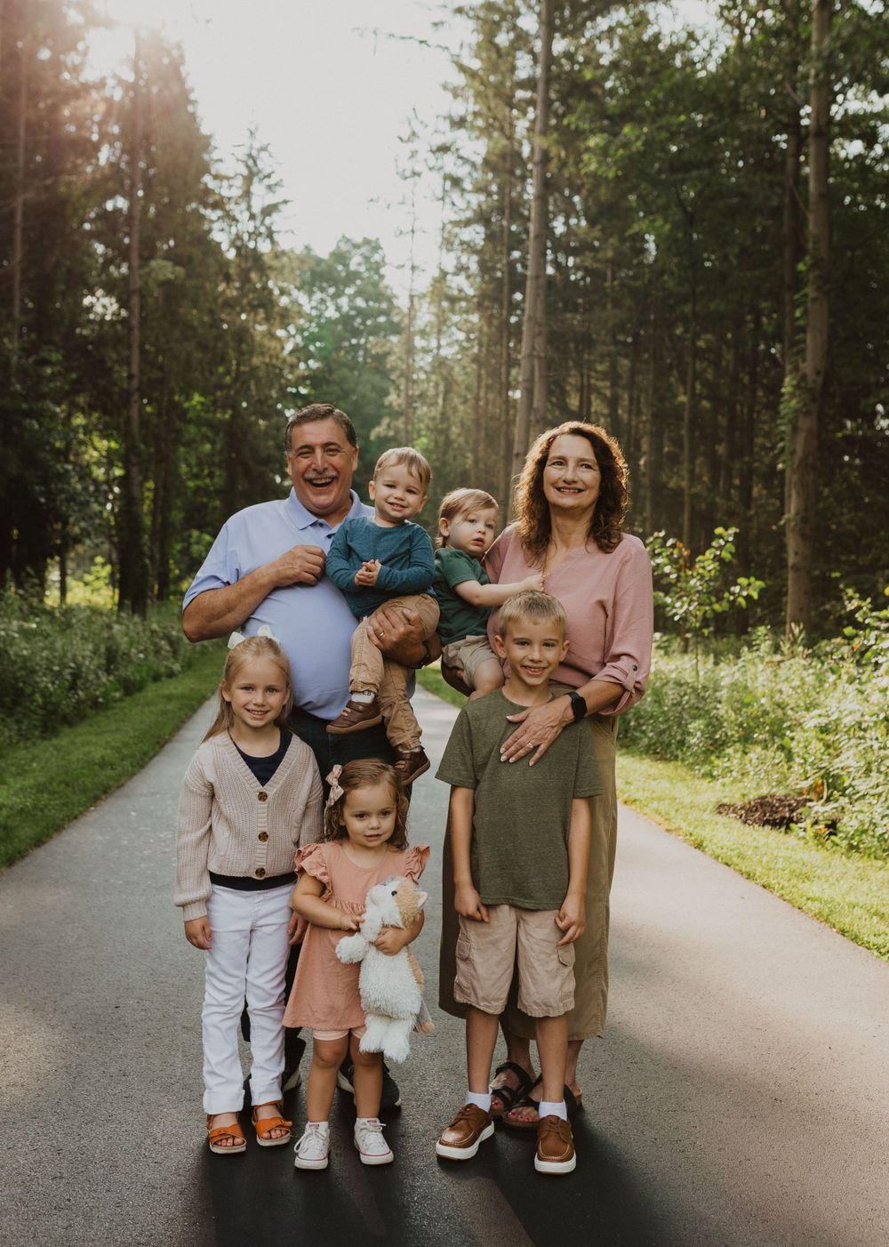 Family of six poses together on wooded path during summer photo session.