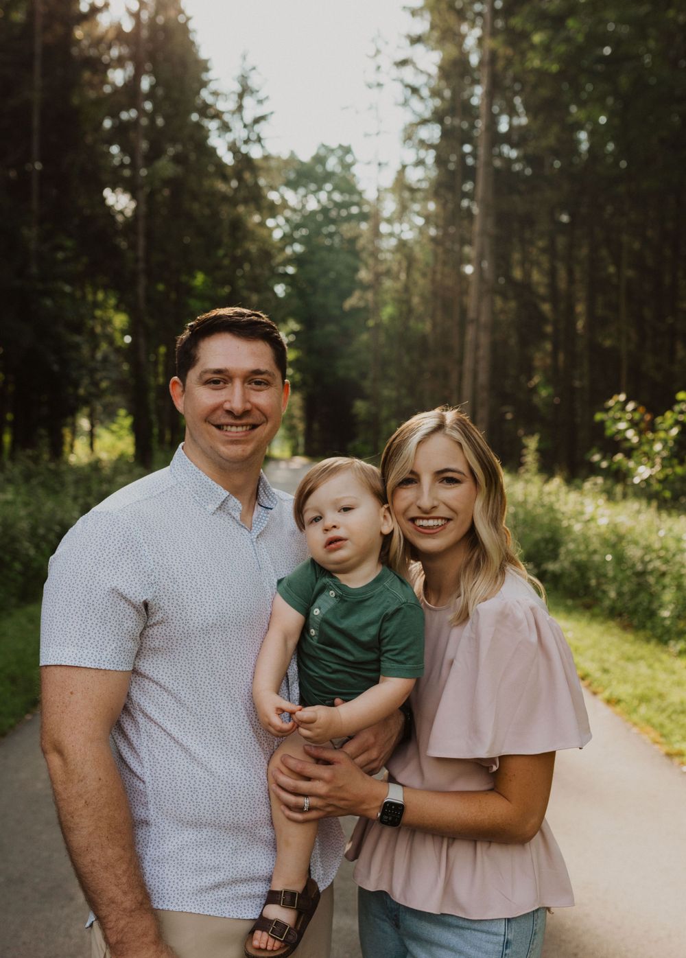 Small family shares intimate moment on forest trail during golden hour.
