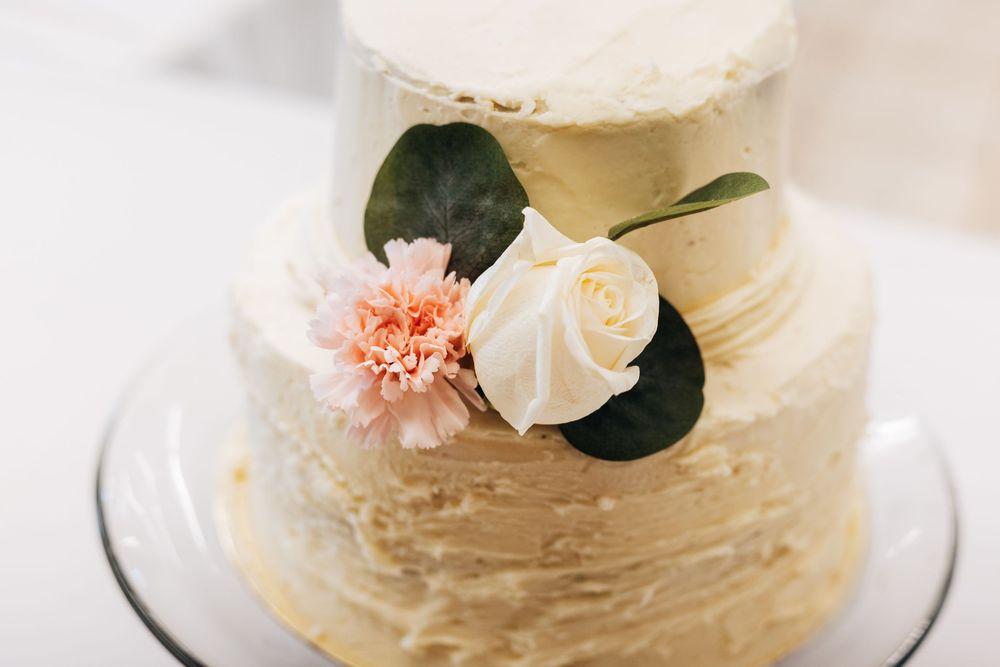 Two-tier white and gold textured wedding cake decorated with a white rose, pink carnation, and green leaves.