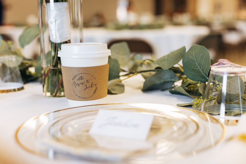 Elegant wedding table setting with gold charger plate, eucalyptus greenery, and personalized coffee cup favor.