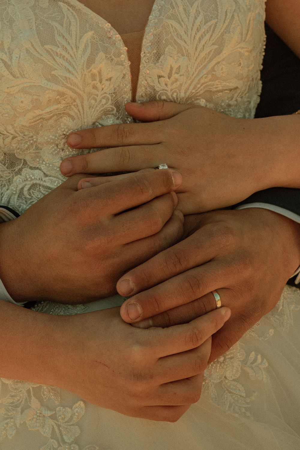 Close-up of newlywed couple's hands with wedding rings, bride in lace dress, groom embracing her waist.