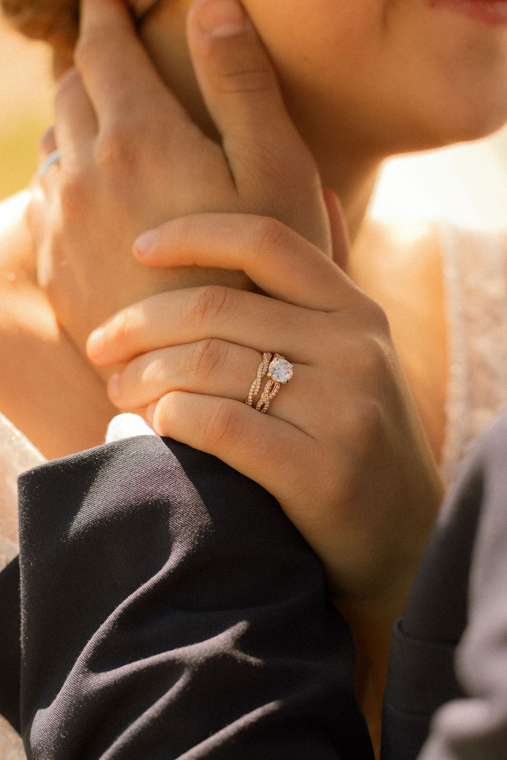 Close-up of a bride's hand adorned with a diamond engagement ring and wedding band, resting on groom's arm.