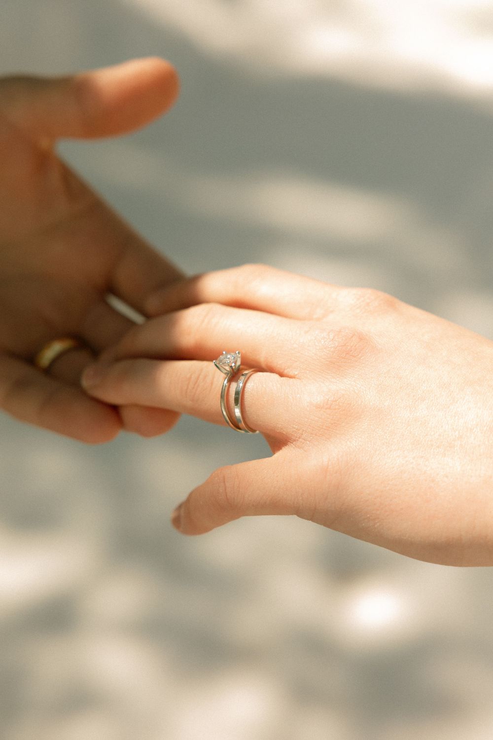 Close-up of two hands touching, woman wearing a diamond engagement ring and wedding band, man wearing a gold band.