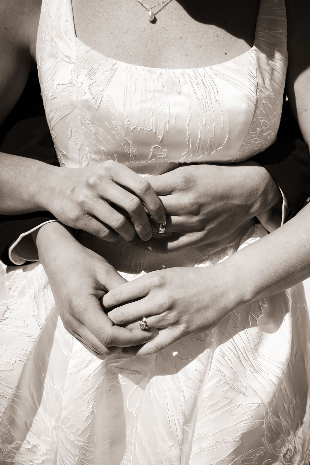 Bride and groom holding hands showing wedding rings in elegant black and white close-up photo.