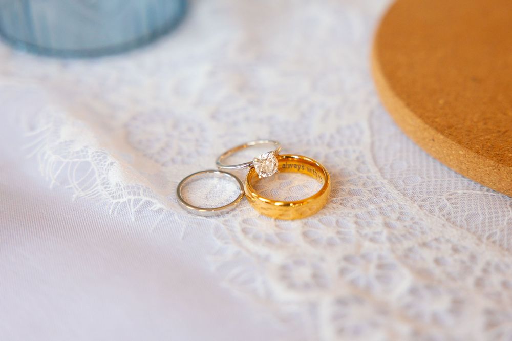Two wedding rings, a gold band and a diamond engagement ring, resting on white lace fabric.