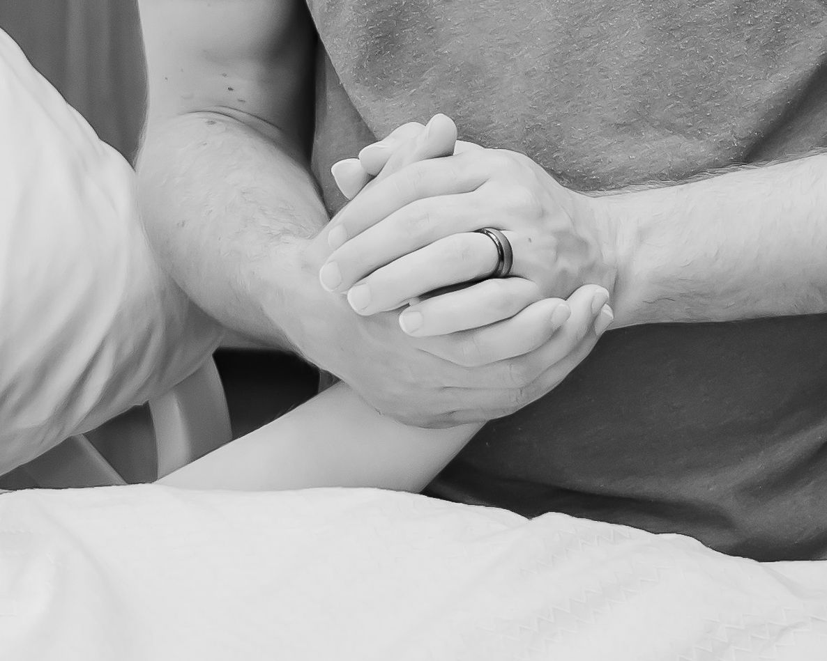 Close-up black and white image of clasped hands with wedding ring showing intimate connection.