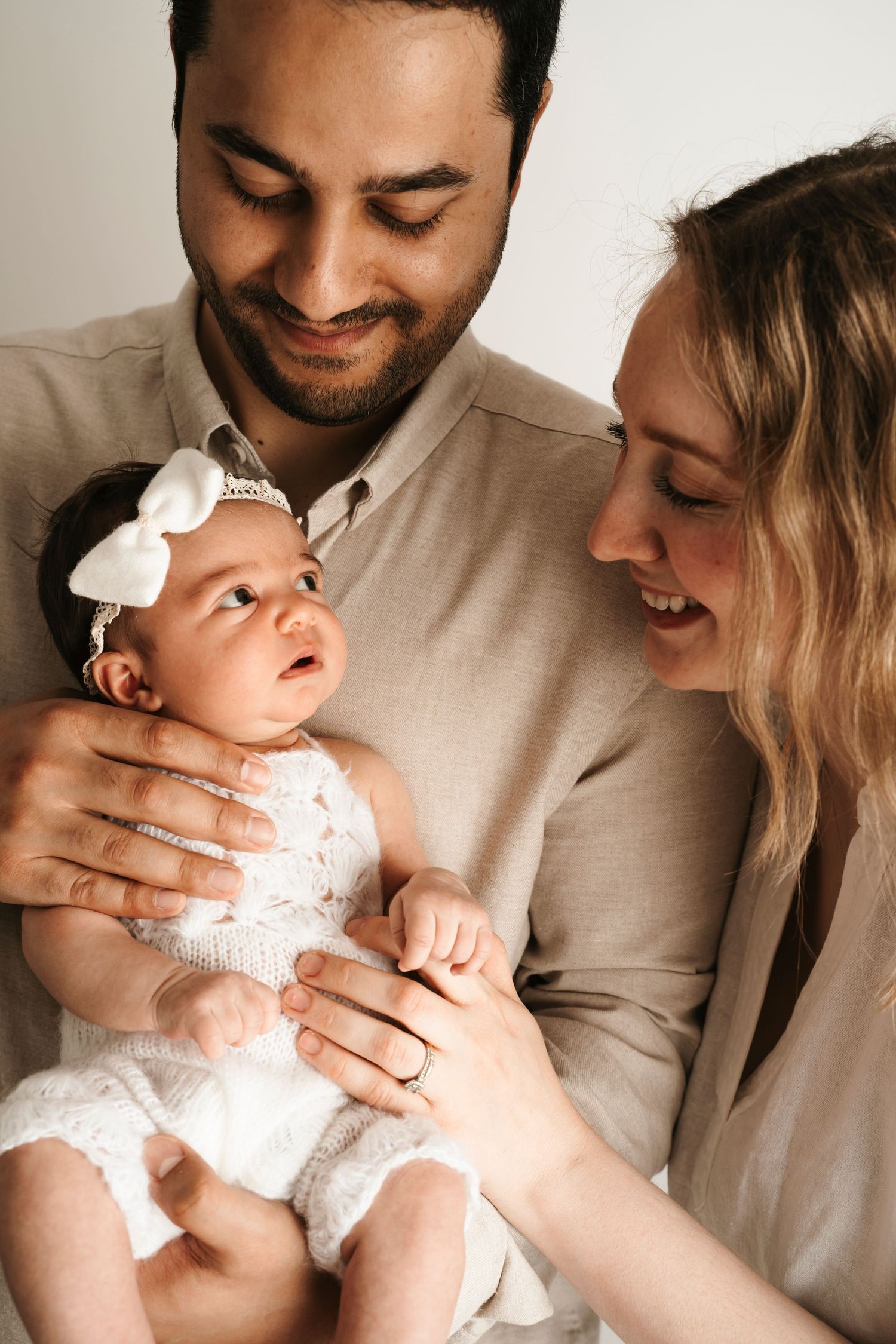 A tender moment as loving parents hold their infant wearing a white lace outfit and headbow. during a storytelling session in Chicago