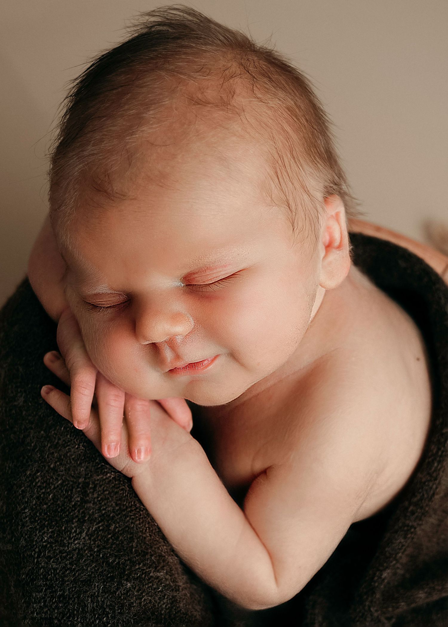 Close up of sleeping baby with hand resting near face on dark fabric.
