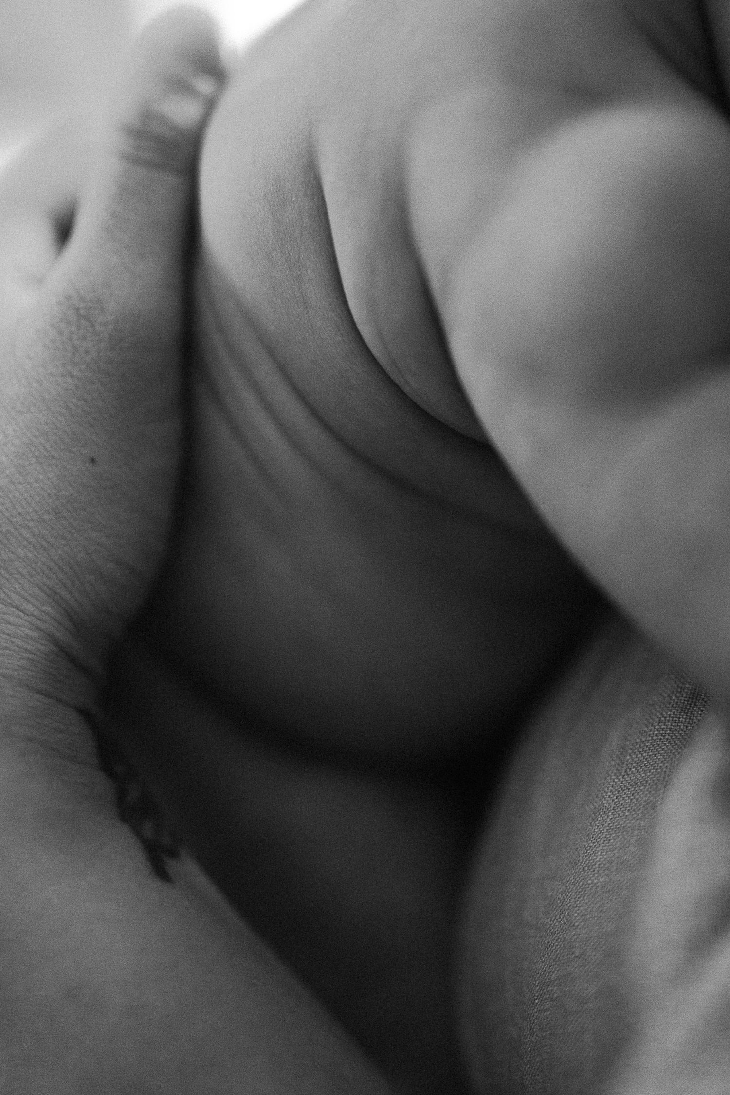 Close-up black and white photo of a newborn baby's tiny feet cradled gently in an adult's hand.