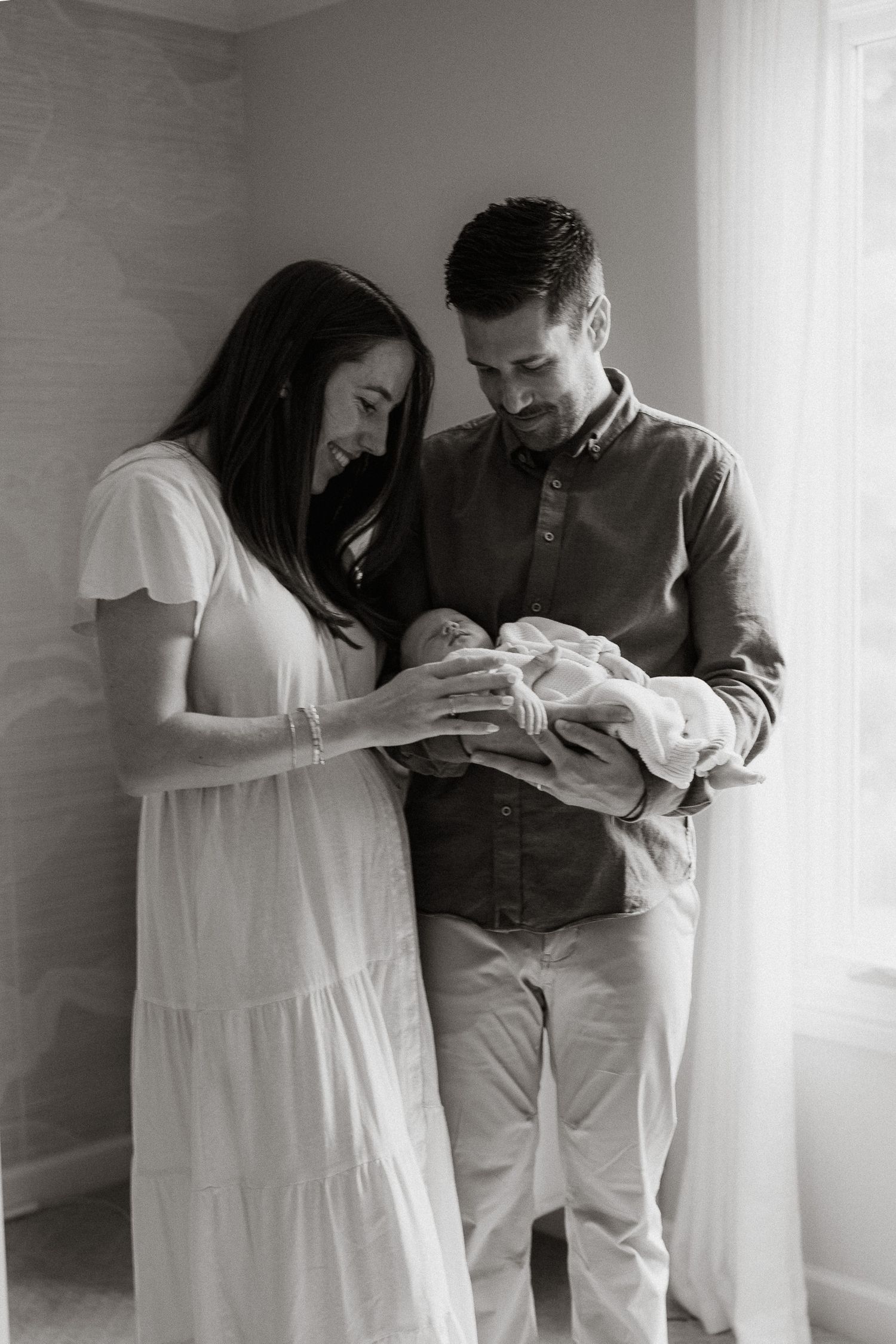 Black and white photo of new parents lovingly cradling their newborn baby together indoors.