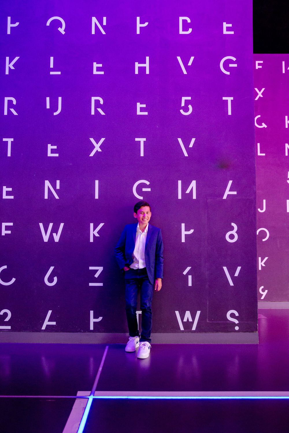 Purple stage backdrop with scattered letters and geometric shapes creating an abstract typographic design.