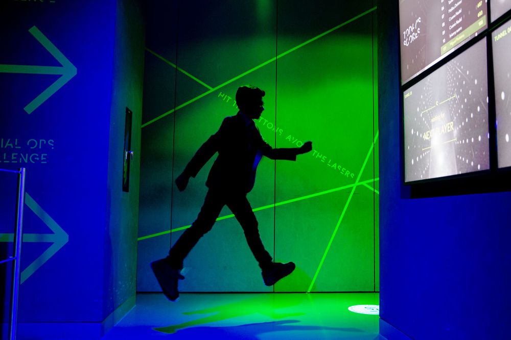 Interactive laser maze exhibit with green and blue lighting creates an immersive obstacle course experience.