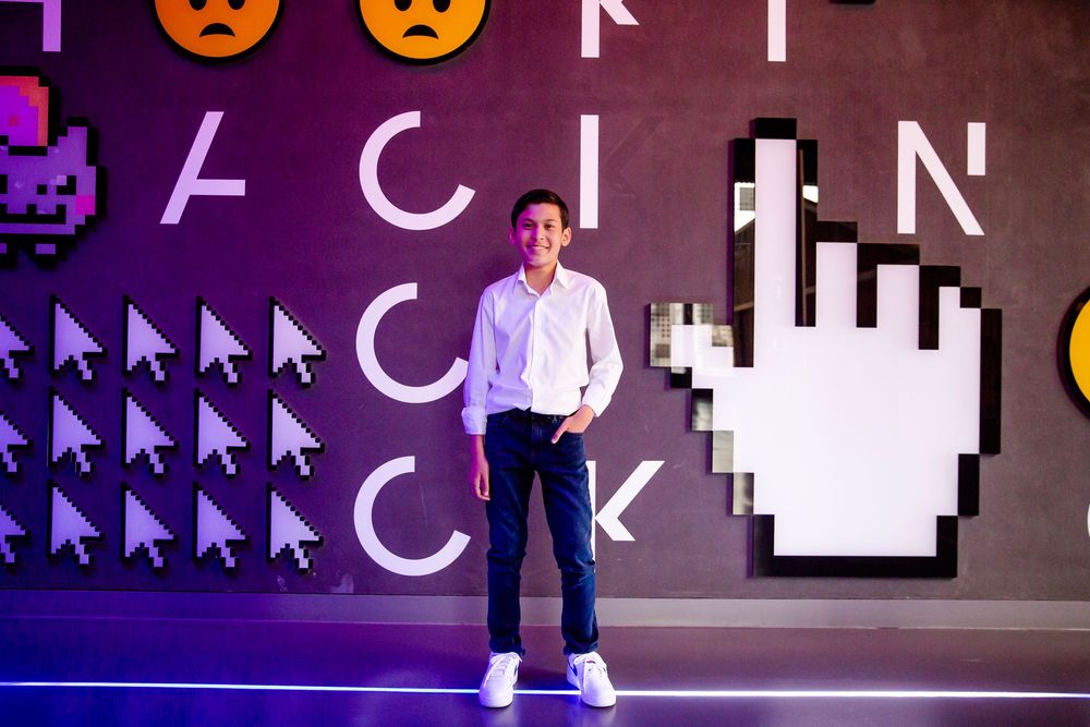 Someone stands against a vibrant purple wall decorated with digital art elements including cursor icons and arrows.