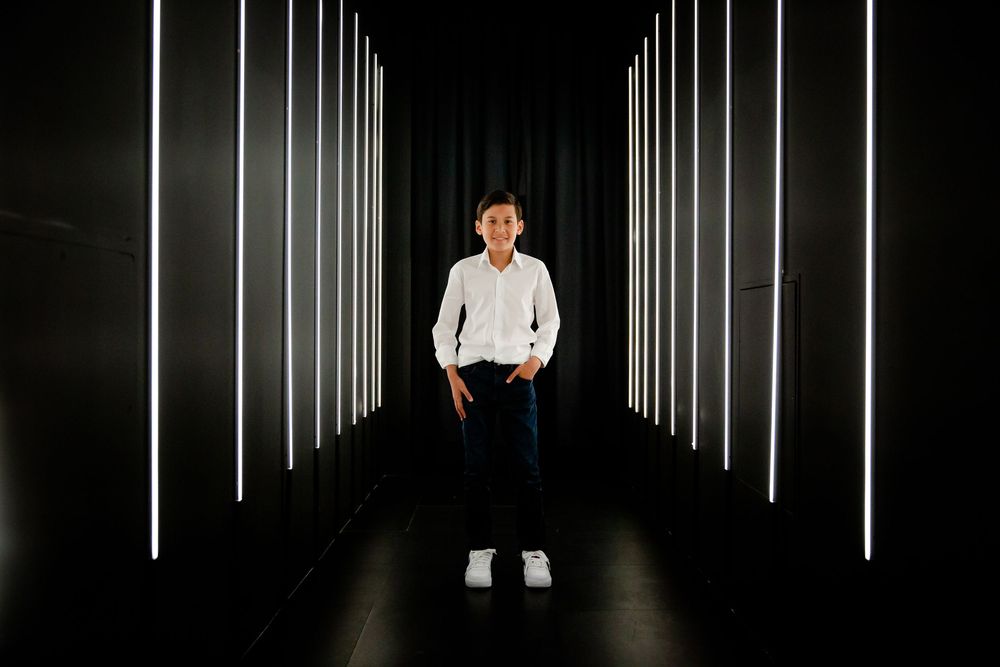 Person stands in dark corridor illuminated by vertical white light strips along walls creating dramatic perspective.