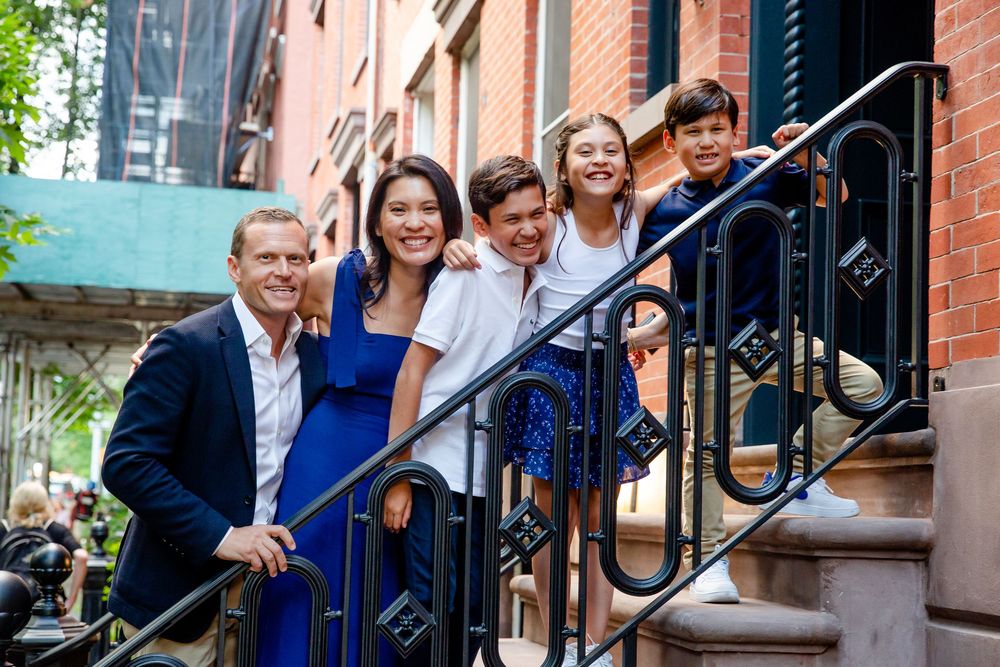 Group of people standing and smiling together on brick building steps with iron railing.