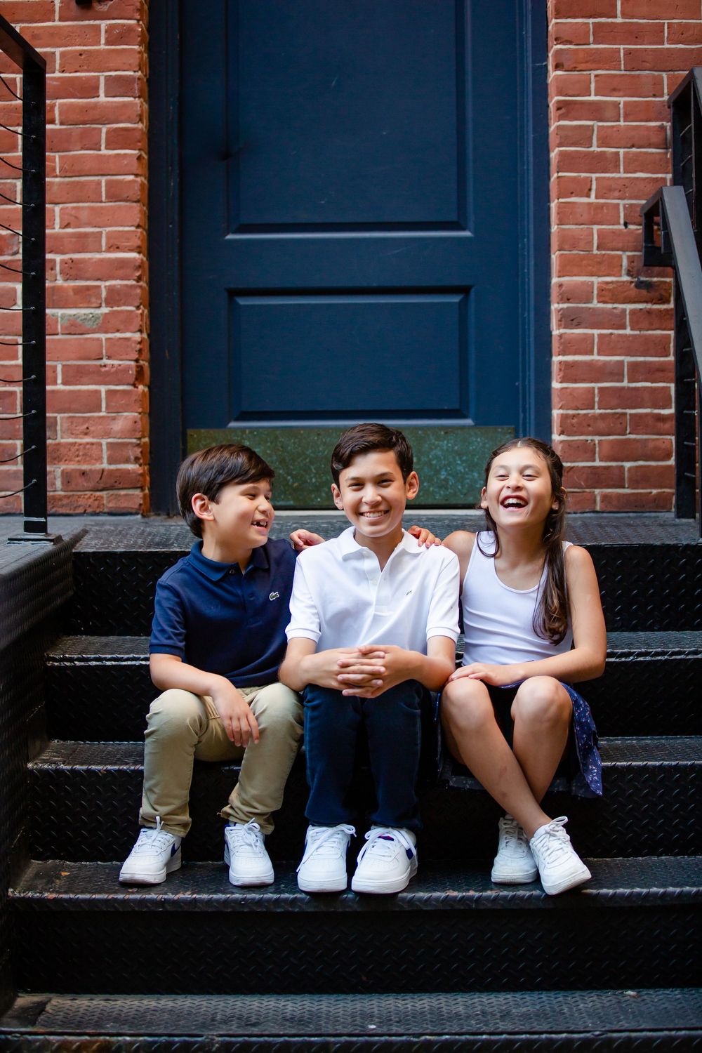 Children sitting and laughing together on brick building steps with navy blue doors.