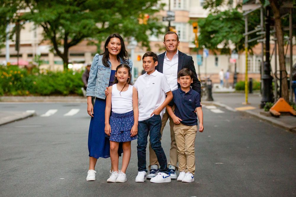 A group of five people wearing casual clothes stand together on a quiet city street.