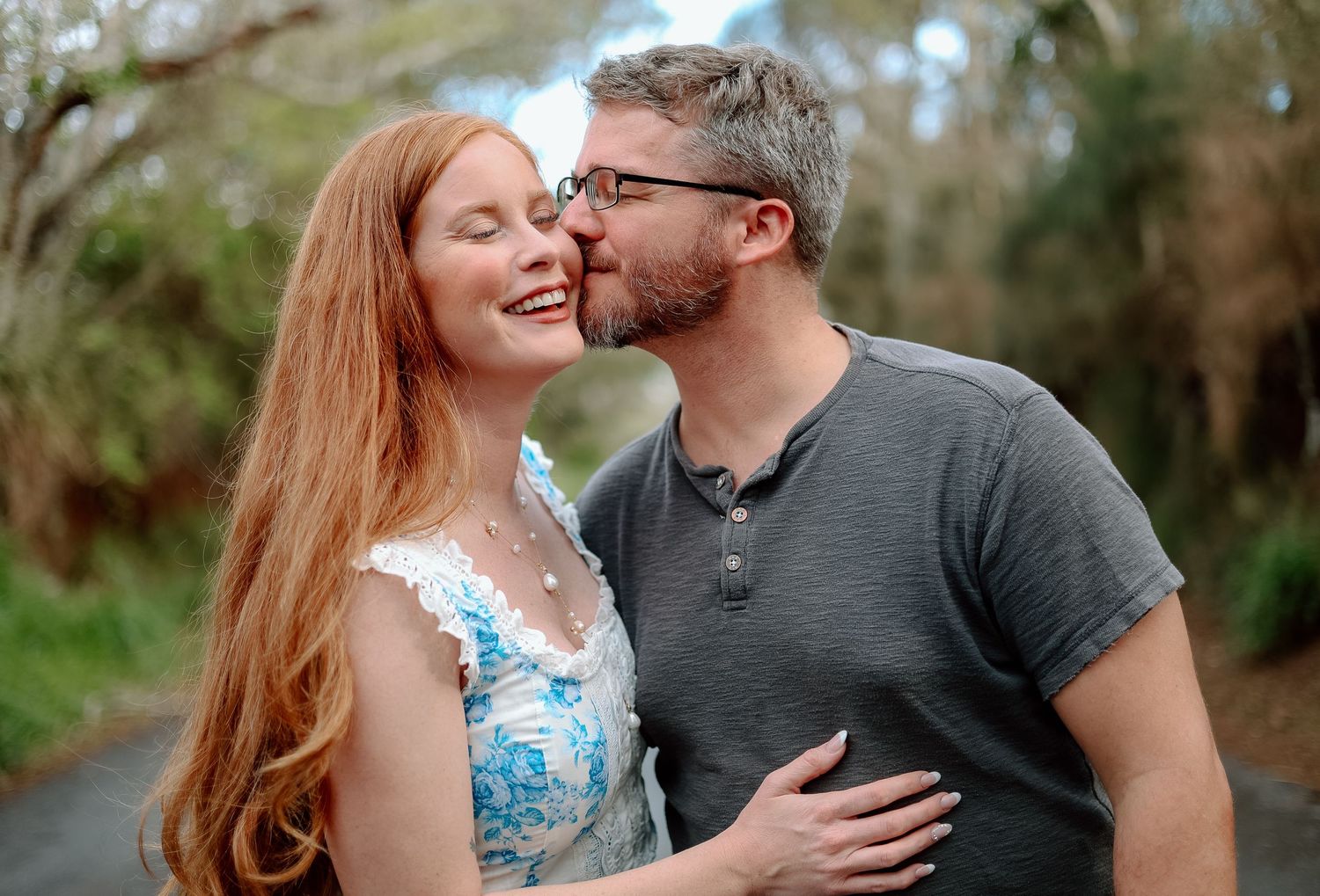 A couple sharing a sweet moment outdoors, with lush greenery in the background.
