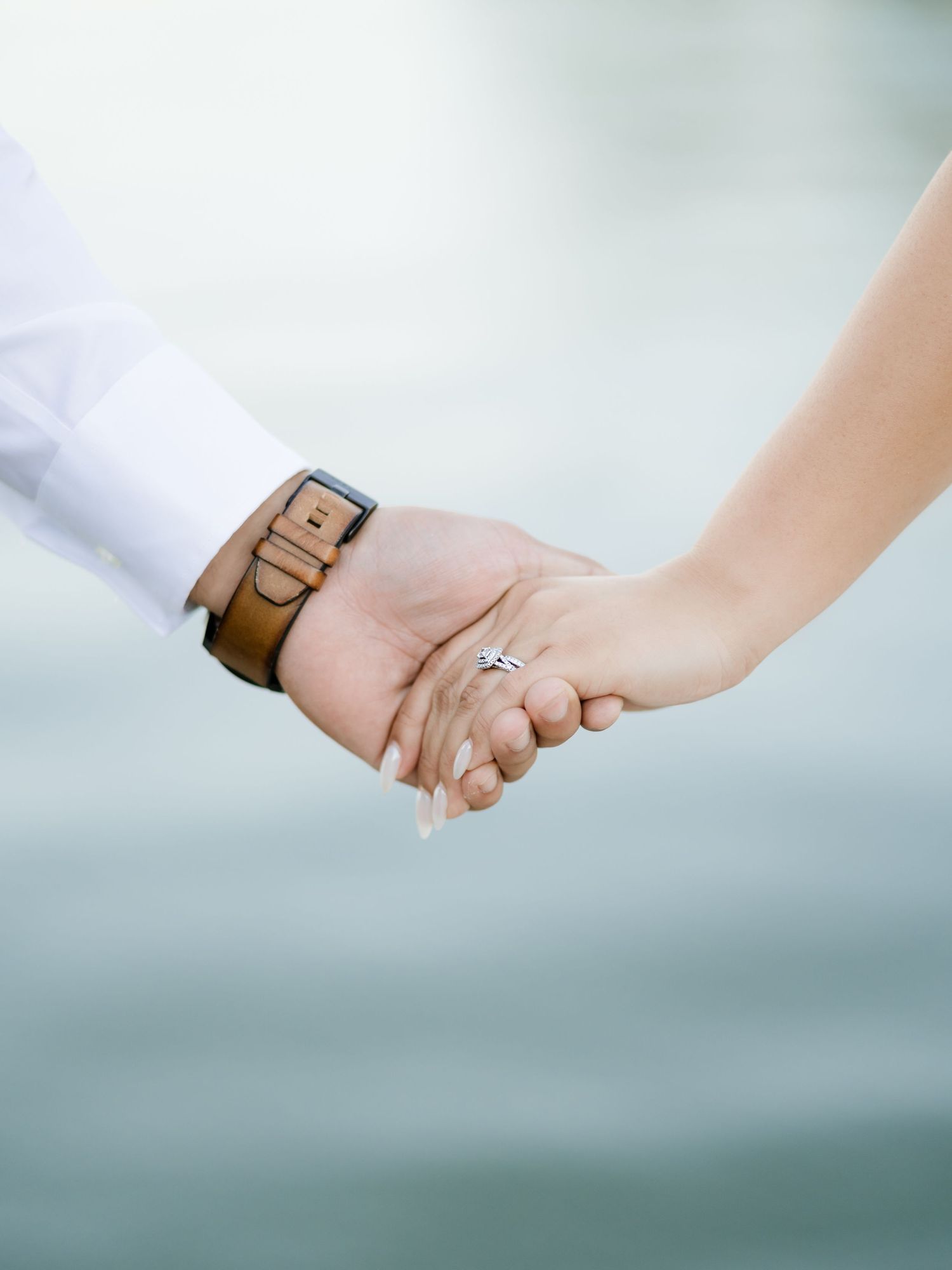 A close-up shot of two hands holding each other, with a diamond engagement ring visible on one hand.