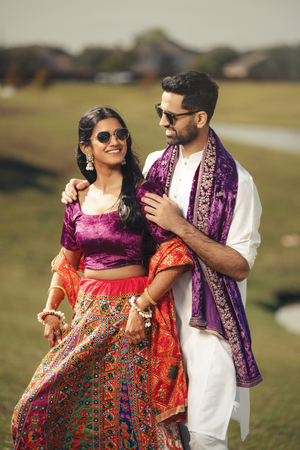 A Houston couple in traditional Indian wedding attire embrace while standing in a grassy field.