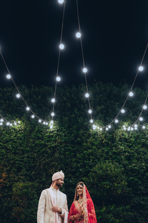String lights illuminate a garden wedding scene in Houston with a hedge wall backdrop creating a romantic outdoor atmosphere.