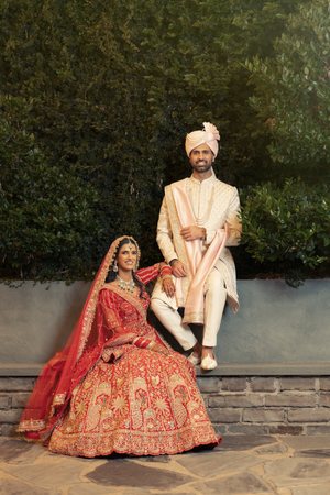 Traditional Indian wedding couple in ornate red and cream outfits pose together for formal portraits outdoors in Houston.