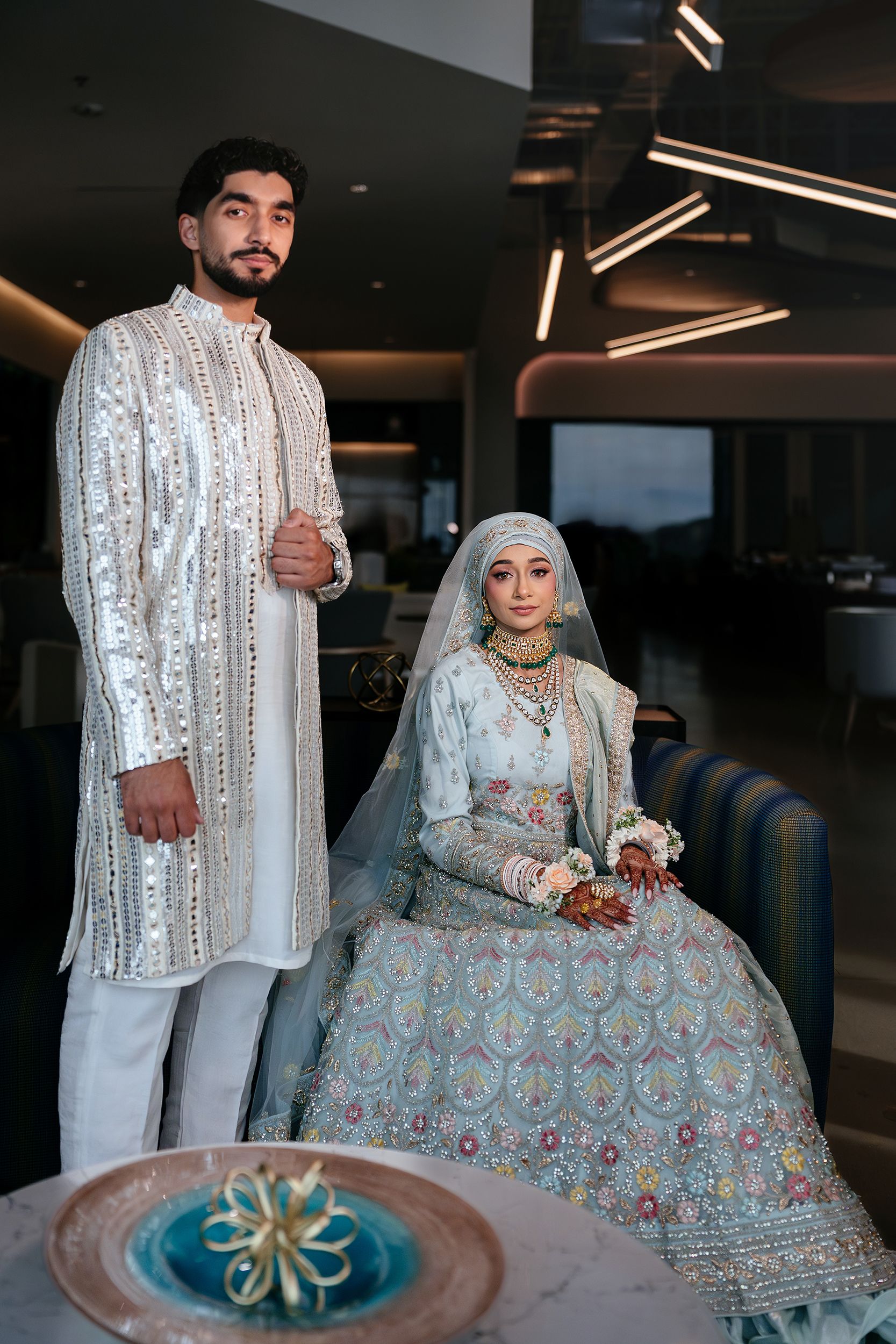 Traditional South Asian wedding couple wearing elegant white and silver embroidered attire with intricate floral details.