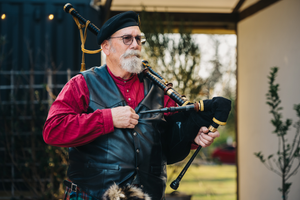 A person in glasses holds a camera while photographing outdoors in a garden setting.