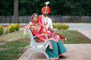 A Sikh couple in Houston in traditional wedding attire sits together on a white bench in front of a Gurdwara.