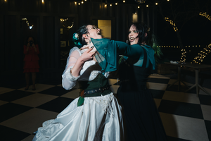 Two people dance together on a checkered floor at a celebration with twinkle lights in the background.