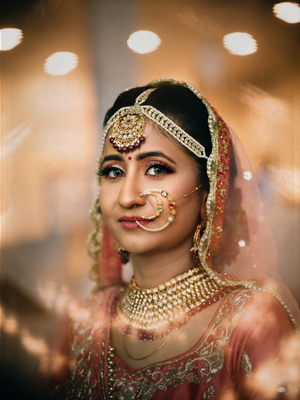 Traditional Indian bridal attire with ornate gold jewelry and nose ring against warm bokeh background.