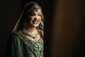 Traditional Indian bride in emerald green lehenga adorned with intricate jewelry and embellishments.