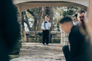 A charming wedding ceremony scene in an outdoor setting with sunlit trees and floral arrangements along the aisle.