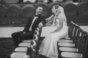 A black and white wedding photo capturing a couple seated on wooden benches in intimate conversation.