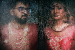 Creative portrait of Indian bride and groom in traditional wedding attire seen through a glass window.