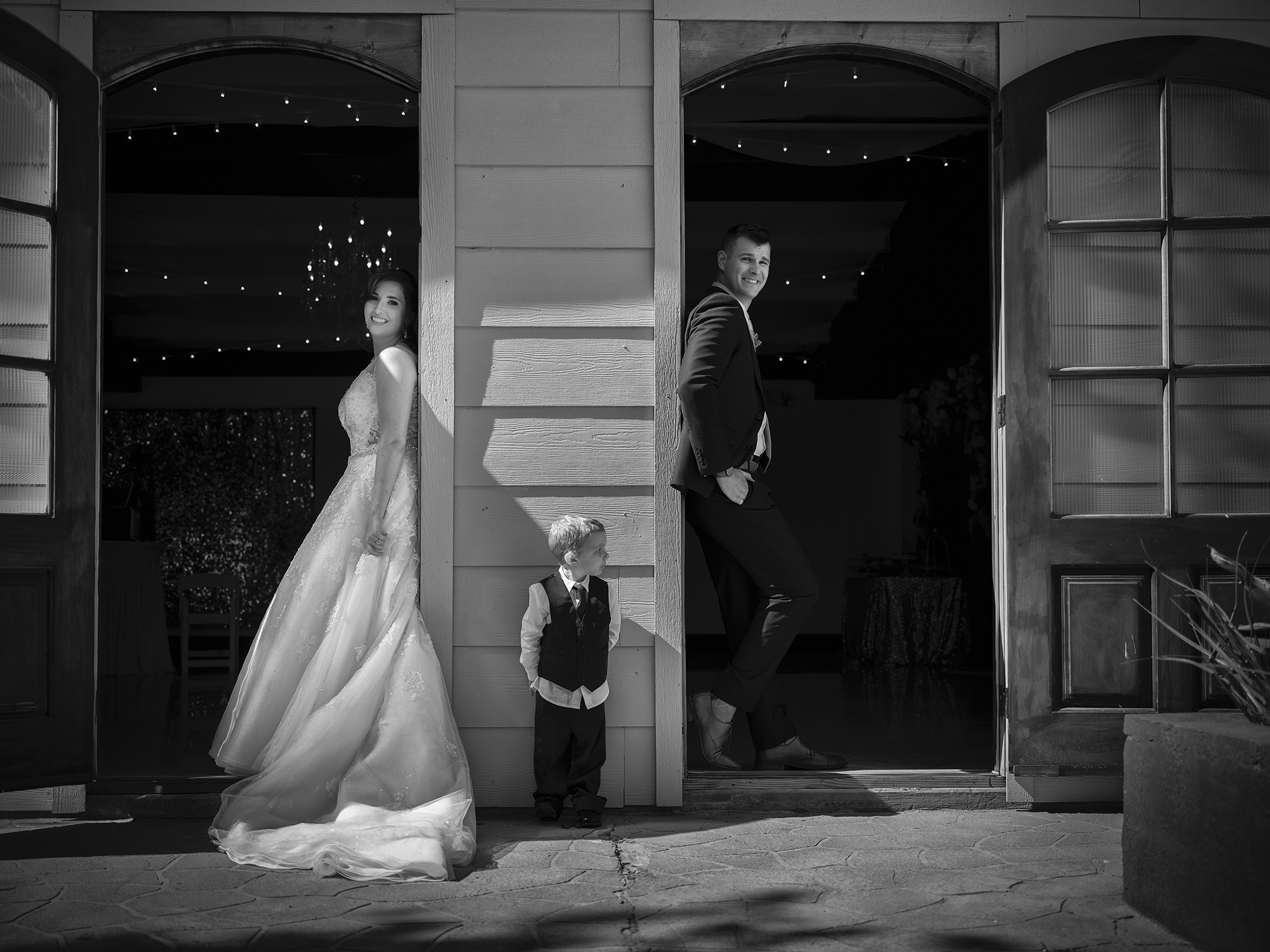 A black and white American wedding photo showing a kid photobombing the couples picture.