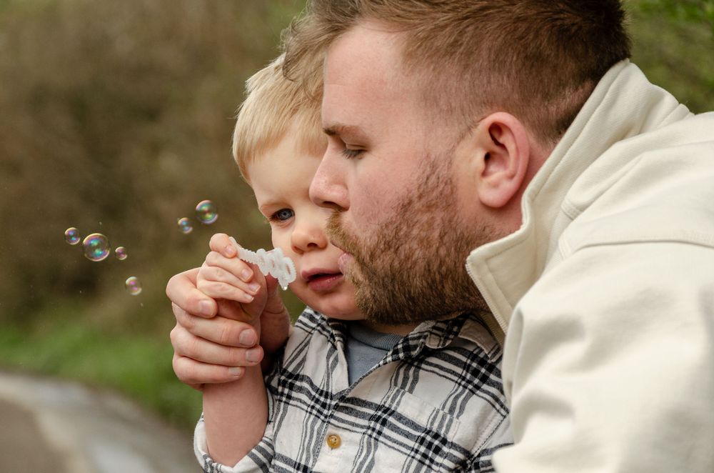 A tender moment between parent and child blowing bubbles together outdoors on a sunny day.