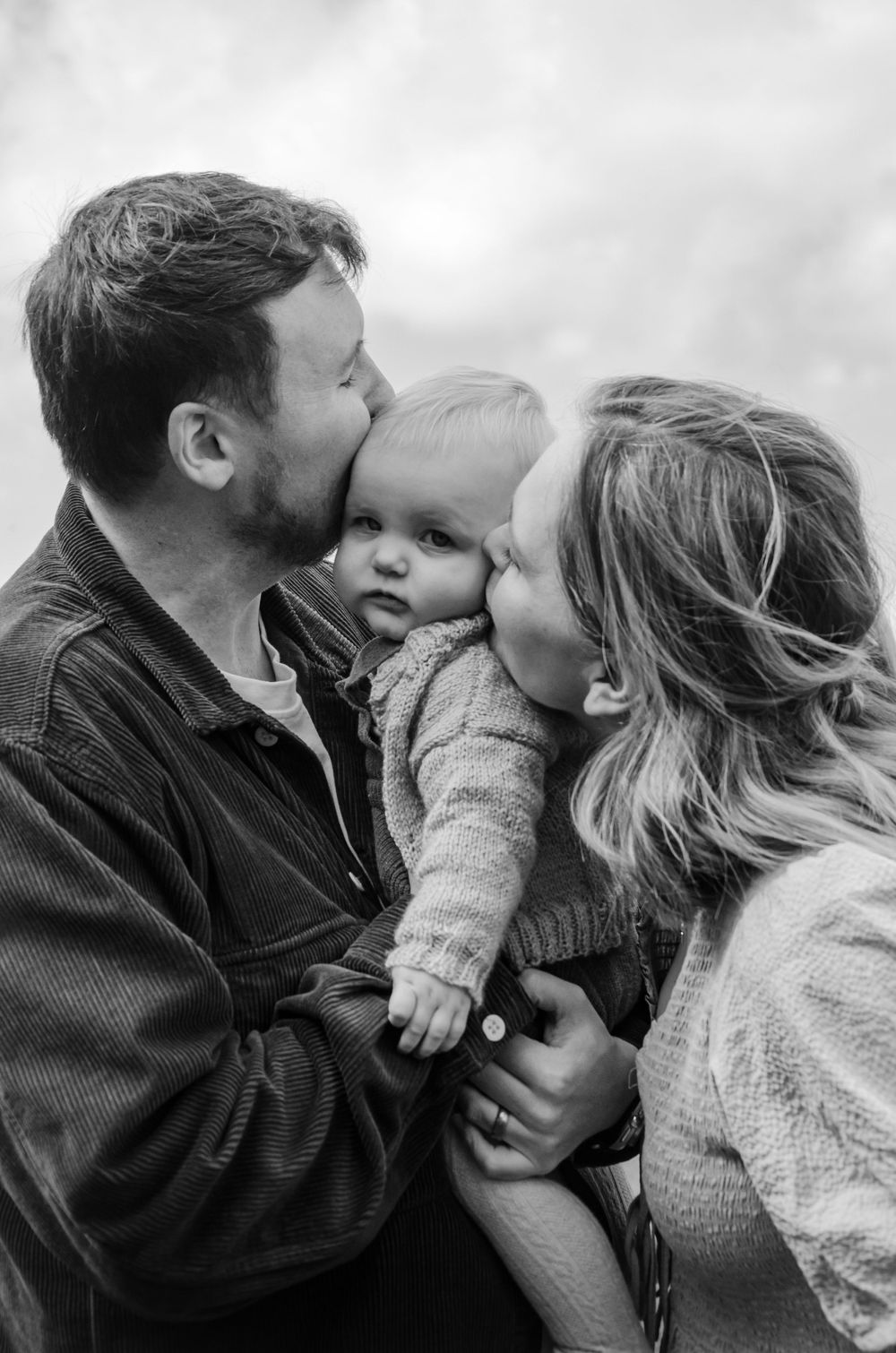 An intimate black and white family portrait showing tender affection between parents and baby.