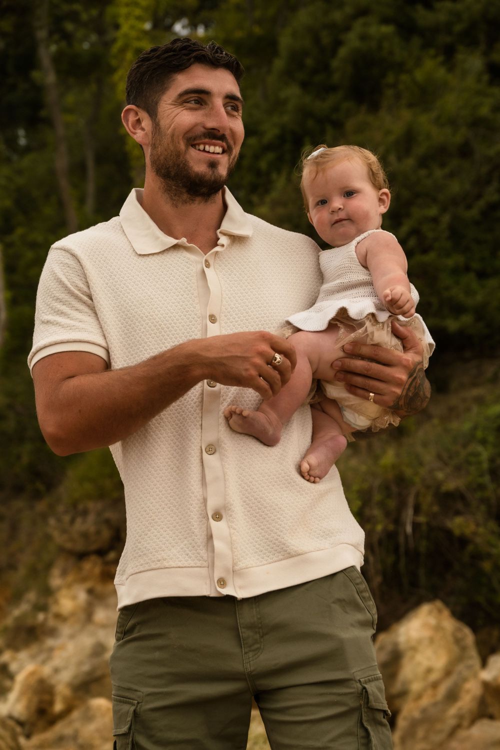 Portrait of a person holding a baby outdoors against a natural background.