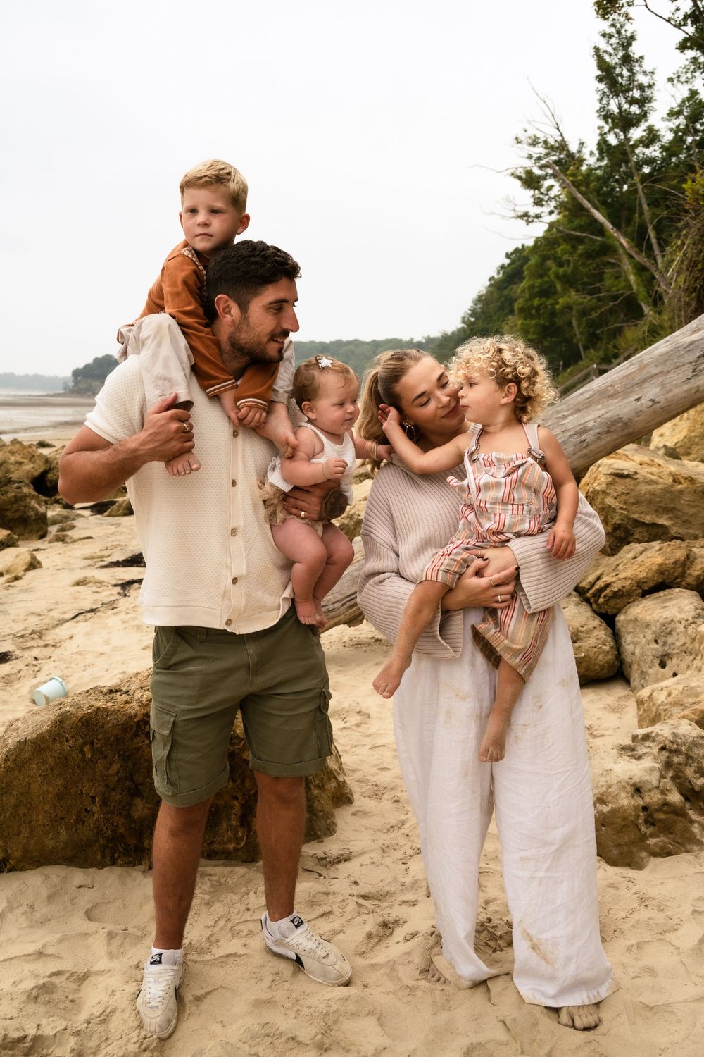 A family shares a joyful moment together on a rocky beach with evergreen trees in the background.