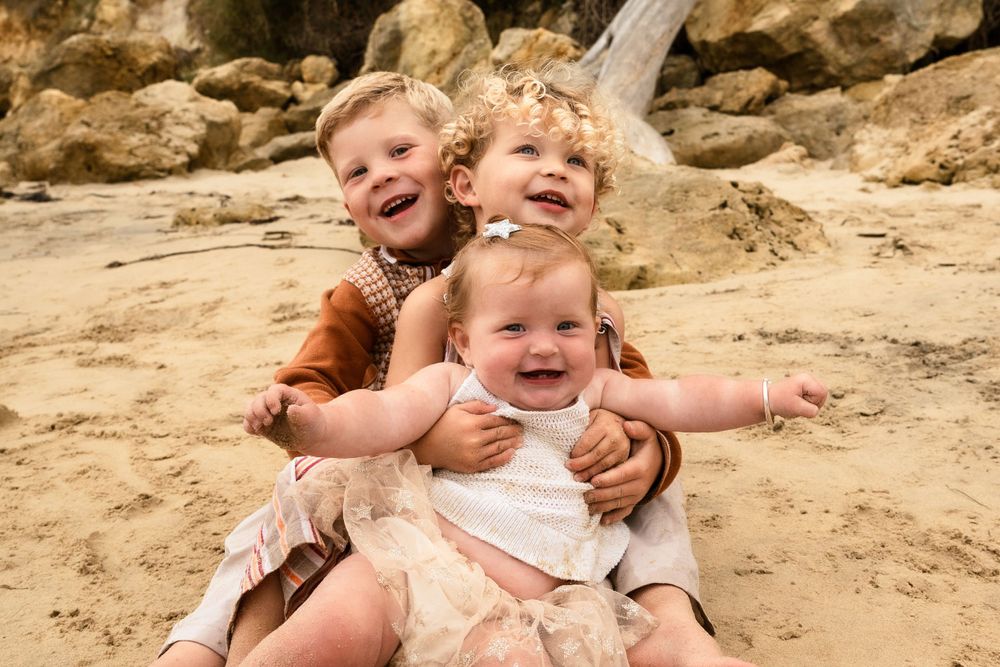 Three young children laughing and playing together on a sandy beach.