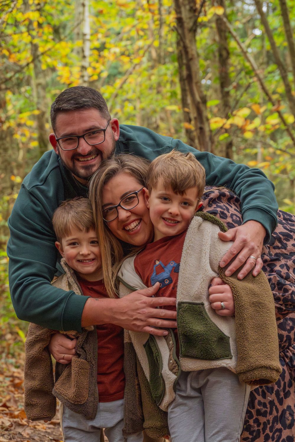 A family embraces and smiles while enjoying a fall day in the woods.