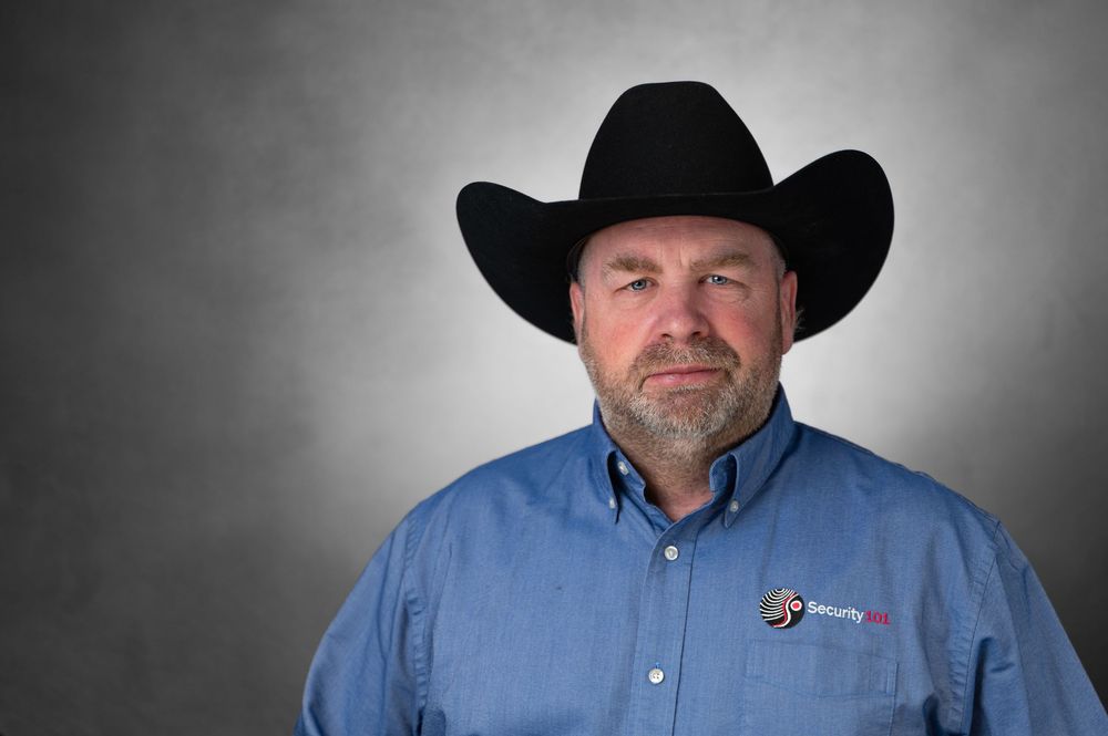 Professional man in black cowboy hat and blue button-up shirt posing for a corporate headshot photo.
