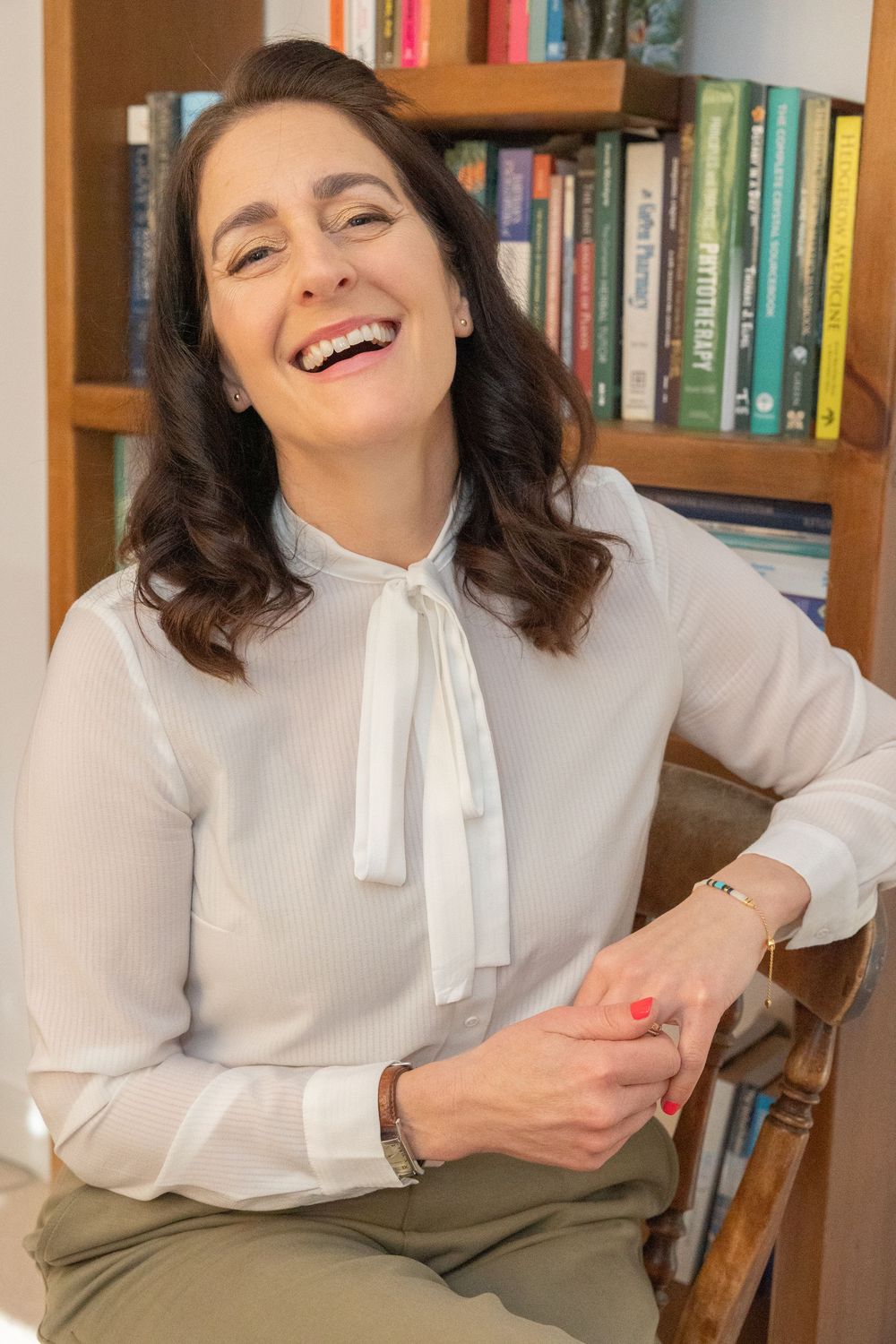 A series of four photos showing someone in a white blouse and olive pants laughing joyfully in front of a bookshelf.