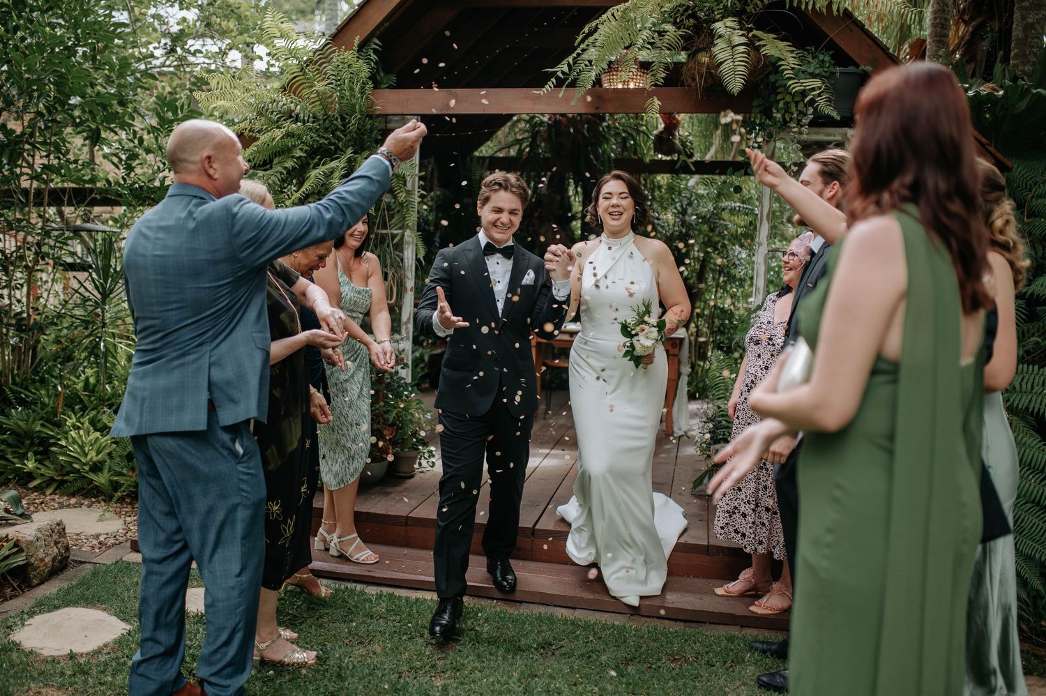 Wedding couple sits with clear umbrellas in a lush garden setting.