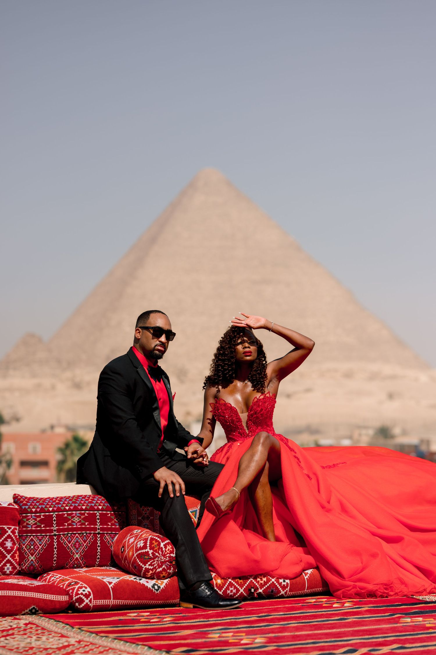 Couple lounges on traditional cushions with the iconic pyramids of Giza silhouetted against the desert sky.